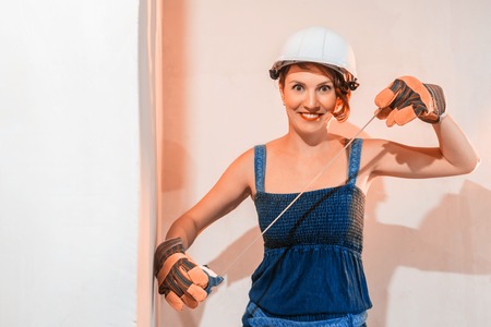 Sexy cute girl who is builder, painter, worker being in a renovated room. Construction roulette in hands of womanの写真素材