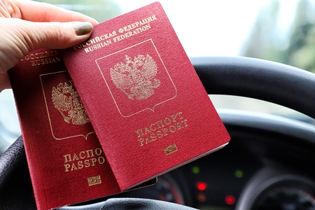 Russian passports in the hand of woman and and the steering wheel of a car with a blurred road and landscape in the background. Concept of travel abroad by car for Russian citizensの写真素材