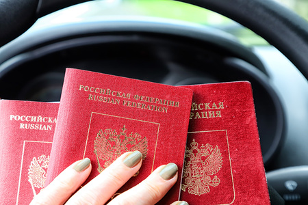 Russian passports in the hand of woman and and the steering wheel of a car with a blurred road and landscape in the background. Concept of travel abroad by car for Russian citizensの写真素材