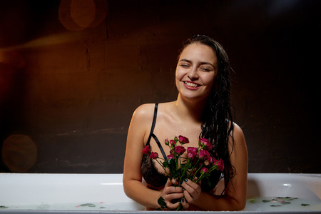 Portrait of young pretty brunette woman in bath with water and flowers. Model during an unusual...