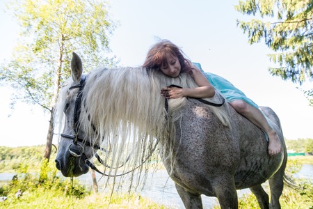 Young girl and white horse near lake in summer sunny dayの写真素材