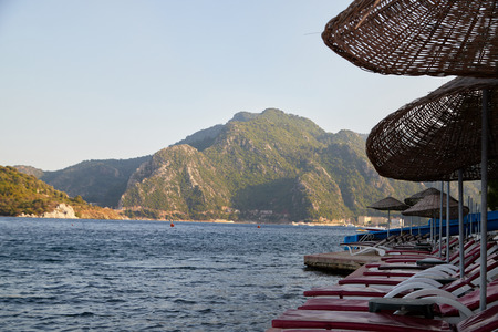 Landscape with sun beds and umbrellas in the foreground and the sea with mountains in the background in a summer dayの写真素材