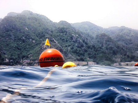 Sea surface with buoys with words No swimming and mountains in the distance. View and shooting from water in a summer dayの写真素材