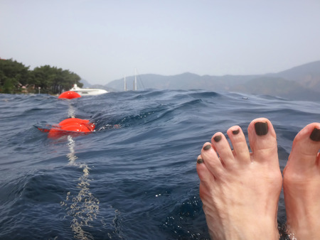 Sea surface with buoys, woman legs under water and mountains in the distance. View and shooting from water in a summer dayの写真素材