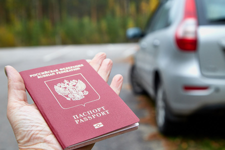 Russian passport in the hand of woman and blur car background. Concept of travel abroad by car for Russian citizensの写真素材