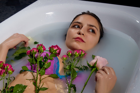 Young pretty brunette woman in bath with water and flowers. Model during an unusual photo shoot in a...