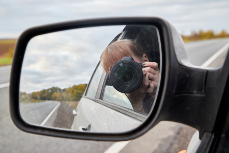 Car mirror, the reflection of the female photographer in it and landscape with field and tree in a summer or in autumn dayの写真素材