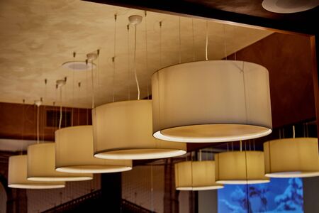 Kirov, Russia - December 28, 2018: Lamps with orange lampshades hang on the ceiling of the cafe. Stylish modern lighting in the interiorのeditorial素材
