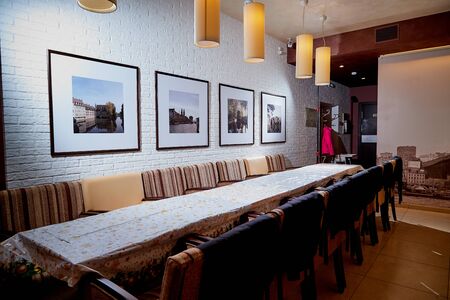 Kirov, Russia - December 28, 2018: Large table in the restaurant in the evening, lamps with light on the celling and pictures on the wallのeditorial素材