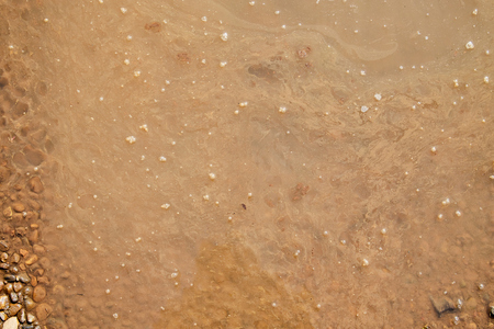 Brown surface of the water in the puddle and the drops and bubbles on it