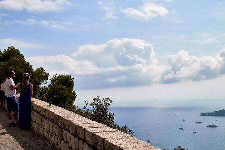 Nice, France - September 23, 2018: Tourist lookin to a view from a high cliff to landscape with greenery to the sea, blue sky, white clouds and ships on a Sunny dayのeditorial素材