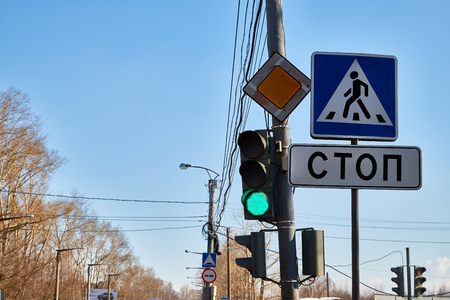 Traffic light with three colors and a sign with the inscription stop in Russian and blue sky with branch of tree in the backgroundの写真素材