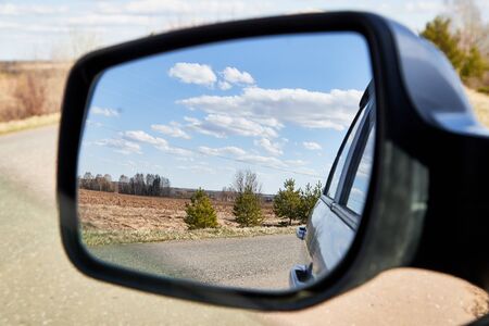 Side view mirror reflection of landscape with road and sky with clouds in sunny spring or autumn day. Russia and russian nature during travel by carのeditorial素材