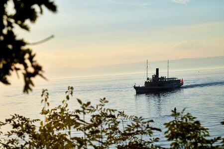View on lake with ship through branch of tree during sunset in summer eveningの写真素材