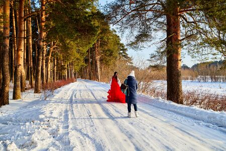 Kirov, Russia - January 05, 2018: Girl in a red beautiful dress during a photo shoot in a winter pine forest on a snowy road in a sunny dayのeditorial素材