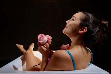 Young pretty brunette woman in bath with water and flowers. Model during an unusual photo shoot in a...