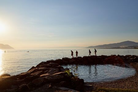 Geneva, Switzerland - September 20, 2018: Tourists on the beach of lake at sunset in a summer eveningのeditorial素材