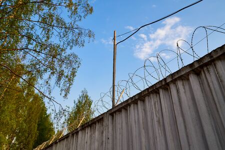 High concrete fence with barbed wire on summer day