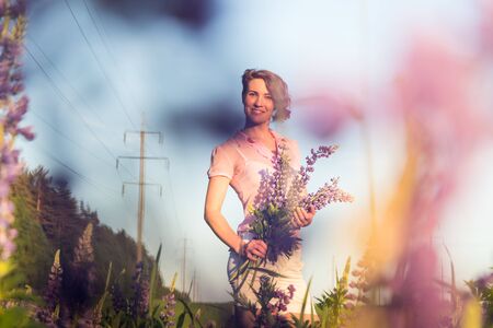 Beautiful girl in a field of purple lupines in a summer dayの写真素材