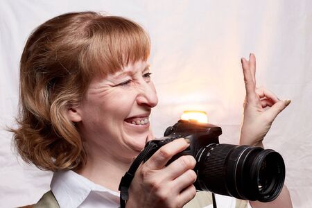 Blonde-haired female photographer with photo camera in her hands on a white background. Woman taking...
