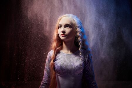 Beautiful teen girl with long blonde curly hair in a dark room with colored lights and clouds of...