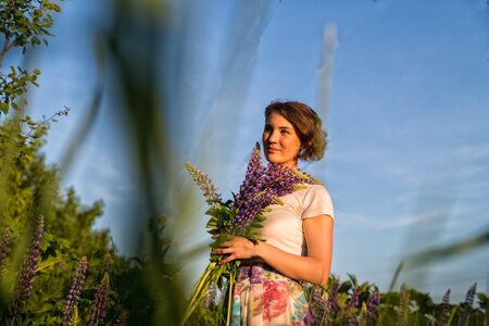 Beautiful girl in a field of purple lupines in a summer day