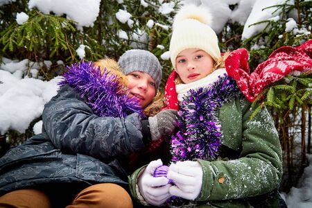 Children sitting at snow forest in a winter day. Teenagers having rest and fun in weekend outdoor....