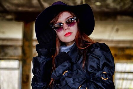 Girl in a black cloak and hat posing in an abandoned, ruined house. Unusual photoshootの写真素材