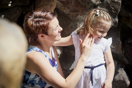 Beautiful mother and pretty small girl on stones in a summer day