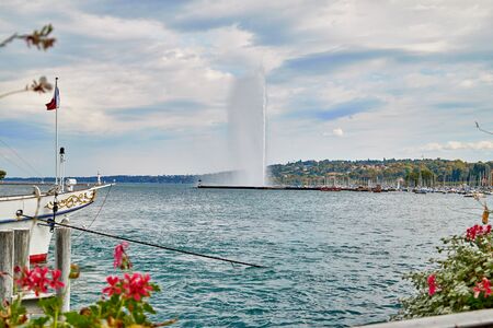Geneva, Switzeland - September 21, 2018: Panoramic view on famous Jet d'Eau fountain through flowers in a nice day with blue sky and clouds in summer, Canton of Geneva, Switzerlandのeditorial素材