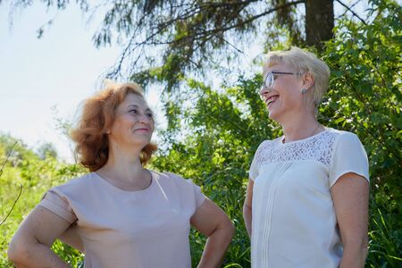 Two female friends having fun on nature. Chubby and slim middle-aged women pensioners in a green field on a Sunny summer day. Two sisters in grassの写真素材