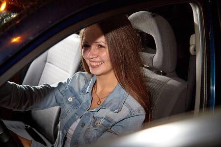 Beautiful young woman in the car at night with light background