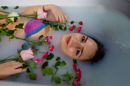 Young pretty brunette woman in bath with water and flowers. Model during an unusual photo shoot in a dark roomの写真素材