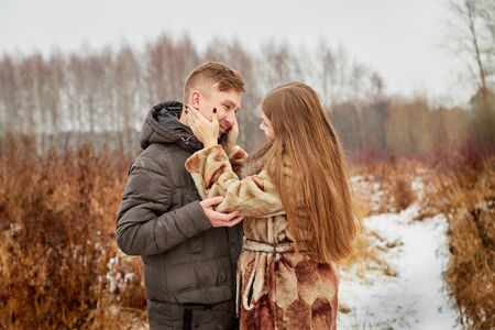 Romantic couple in love on autumn or winter walk outdoors. Natural scenery. Field with yellow grass and path covered with snowの写真素材