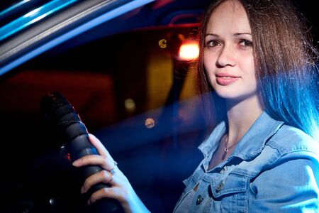 Beautiful young woman in the car at night with light backgroundの写真素材