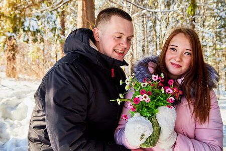 Celebration of St Valentine's day. Happy and beautiful young couple in love are walking together outdoors in winter city park, hugging each other. Flowers as a giftのeditorial素材