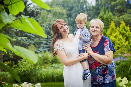 Happy family consisting senior lady grandmother, young mother and small son in garden or park in a summer or autumn dayの写真素材