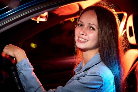 Beautiful young woman in the car at night with light background