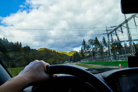 View of the road with a beautiful mountain landscape from the car window in a nice summer or autumn day. Woman's hand on the steering wheel. Female driver seeing beautiful landscape during travelの写真素材