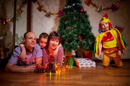 Family consisgitng mother, father and two brothers in carnival costumes at Christmas or new year near the Christmas tree in the room. Mom, dad and boys indoor posing togetherの写真素材
