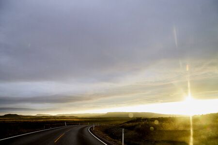 View on yellow sunset and clouds from the car front window and the glare on the glass. Driving car during sunshine in the tundra in Norway. Background of nature landscape and grey roadのeditorial素材