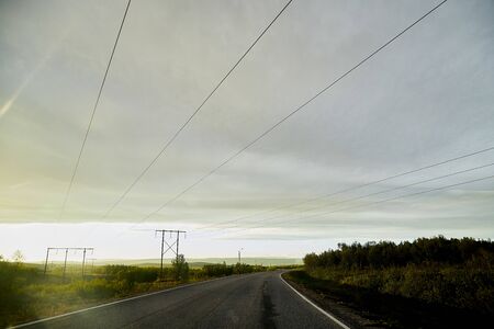 View on yellow sunset and clouds from the car front window and the glare on the glass. Driving car during sunshine in the tundra in Norway. Background of nature landscape and grey roadのeditorial素材