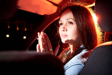 Beautiful young woman in the car at night with light background