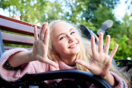 Pretty teenage girl 14-16 year old with curly long blonde hair in the green park on the bench in a summer day. Beautiful outdoors portraitの写真素材