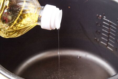 Cooking at home. A bottle of sunflower oil in the hand and pouring oil into the containerの写真素材