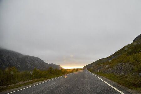 View from car cabin on wet asphalt road during rain and drops on front window. Pity grey landscapeの写真素材