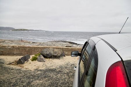 Car on the beach of sea, river or lake with rocks on a cloudy day in a summer, spring or autumn. The fjord of Northern Norwayの写真素材