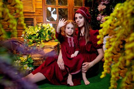 Easter. Family models in rural wooden interior with flower in studio. Mother and daughter in maroon...