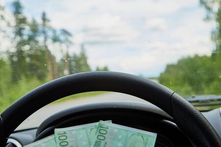 Euro banknotes in a woman hand inside of a car and road with nature outside
