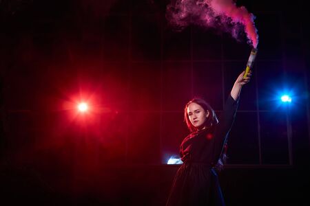 Teenage chubby girl with colored smoke torch in hand during photoshoot with colored smoke at night...